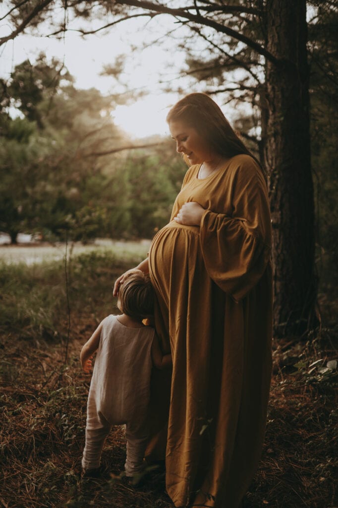 Maternity Photographer, an expectant pregnant mother stands besides her toddler under a tree outside