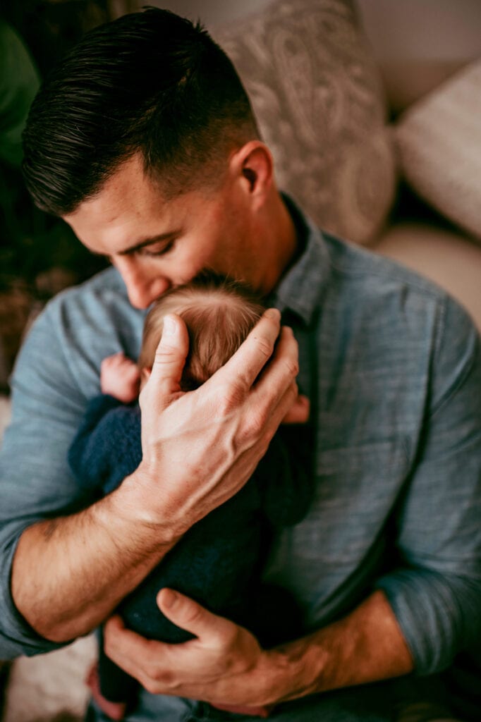 Newborn Photographer, a father holds his baby close to his chest