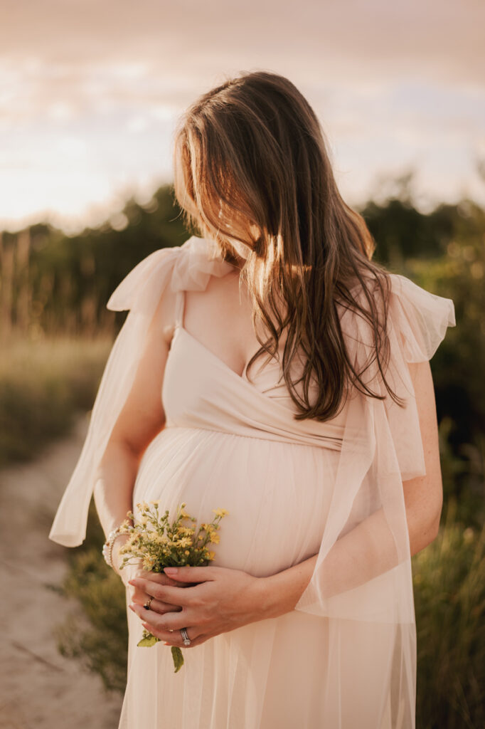 Maternity Photography, woman in long flowing cream pink dress holding a small bouquet of wild flowers